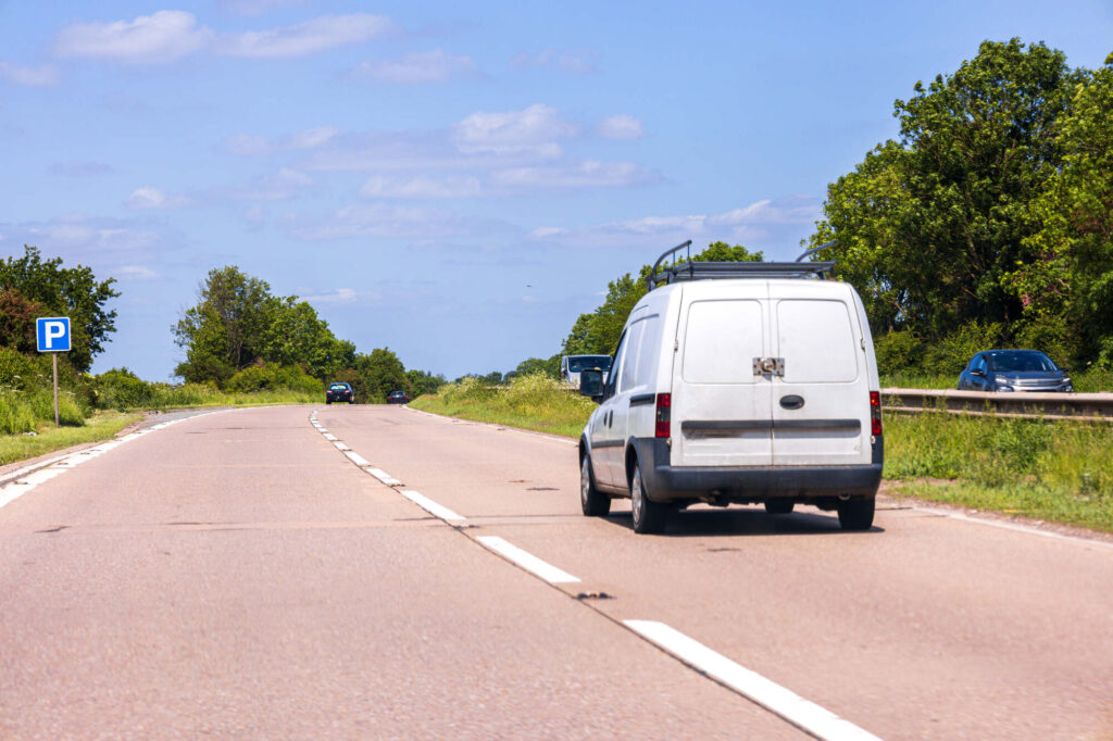 A single white van driving on an empty winding road